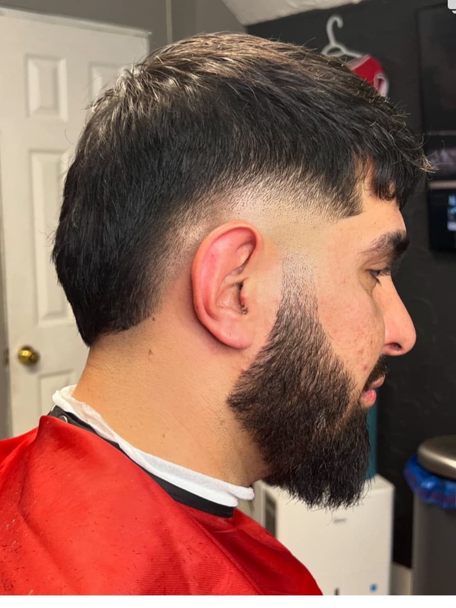 Burst fade arcing around the ear with a textured top and a full beard