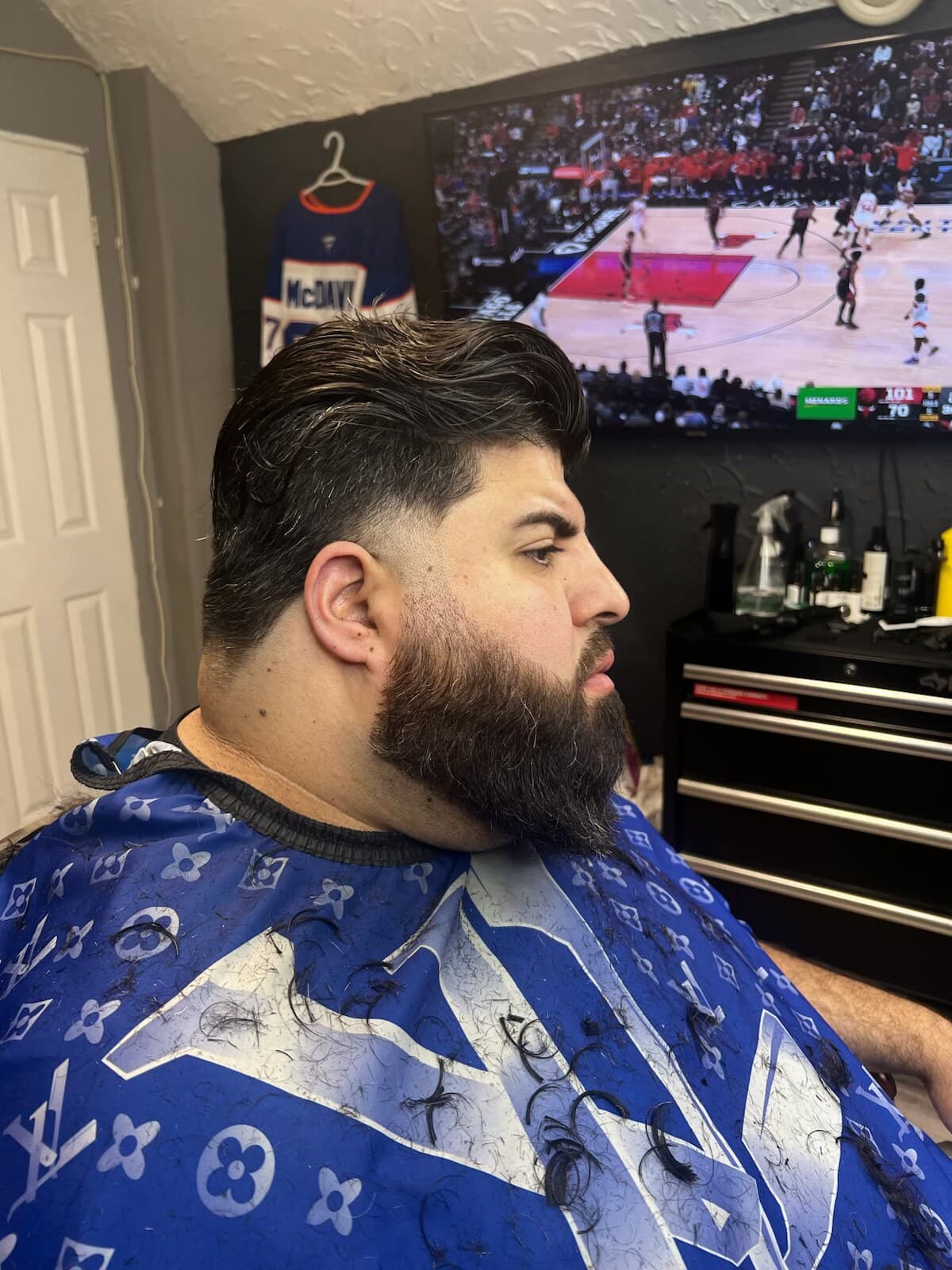 A full beard sculpted to the jaw with a clean cheek line, over a low fade